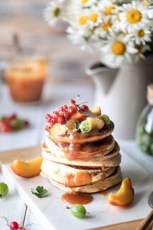 Cornmeal pancakes with salted caramel served with berries and fruits on a white wooden background. Rusticの写真素材