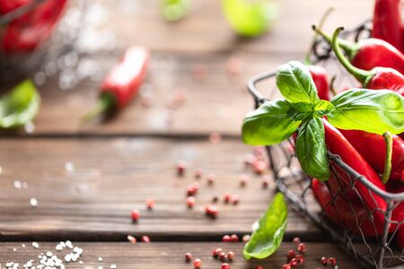Red chili peppers with a sprig of basil in a wicker metal basket on a wooden backgroundの写真素材