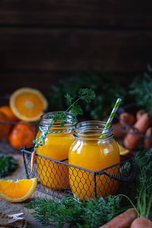 Healthy food. Carrots and carrot juice with orange in a glass jar in a metal basket on a dark wooden backgroundの写真素材