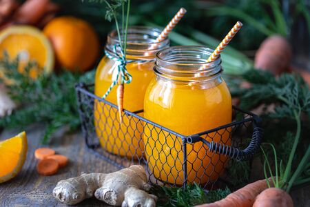 Healthy food. Carrots and carrot juice with orange ginger in a glass jar in a metal basket on a dark...