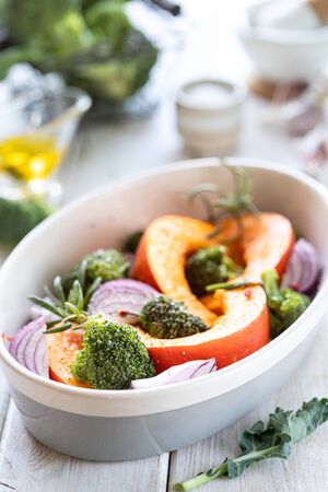 Traditional autumn pumpkin dishes. Grilled roasted pumpkin with spices, olive oil, herbs, broccoli and onions. On a baking sheet, on a rustic wooden white backgroundの写真素材