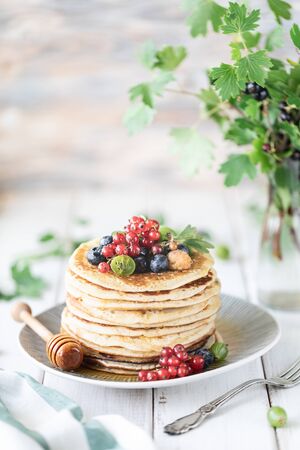 Pancakes with fresh berries of raspberries, currants, blueberries, with honey and tea. copy space.の写真素材