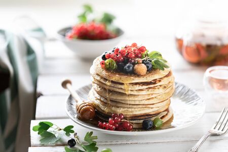 Pancakes with fresh berries of raspberries, currants, blueberries, with honey and tea.