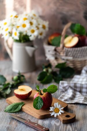 Homemade compote of summer apples on a wooden table by the window. Basket of apples. Wild flowers of the chamomile in the jar.の写真素材