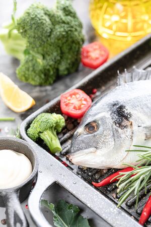 One raw dorado fish with spices, lemon and parsley in a black grill pan on a white concrete background. Healthy eating and tasty culinary concept.の写真素材