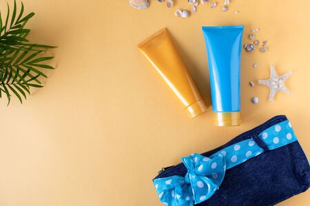 Suncream bottles, glasses, starfish, palm leaves on a yellow background. Beauty and care in the...