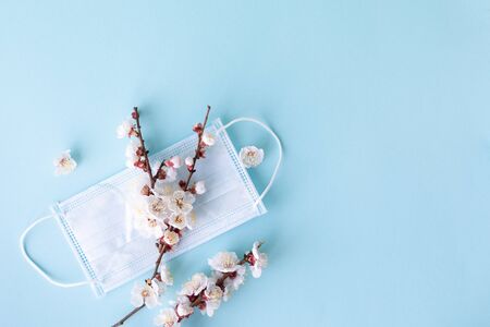 Medical concept on a blue background. Medical mask and a branch of spring flowers as a symbol of...