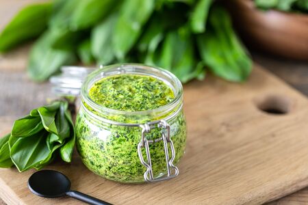 Wild leek pesto with olive oil and parmesan cheese in a glass jar on a wooden table. Useful...