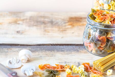 Different types of italian pasta in glass jars on a yellow wooden table.の写真素材