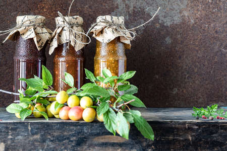 Three glass bottles of assorted Georgian tkemali sauce with ingredients on rustic wooden table