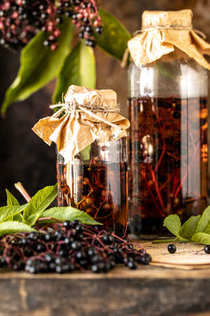 Fresh black elderberry syrup in a glass bottle on a wooden table.