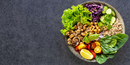 Quinoa, mushrooms, lettuce, red cabbage, spinach, cucumbers, tomatoes, a bowl of Buddha on a dark...