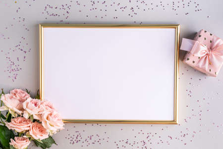 Festive frame with pink roses and a gift on a gray background. Top view, flat lay. Copy space....