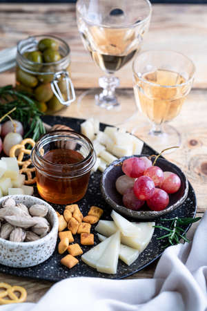 Assorted cheeses on a dark plate on a wooden table. Cheese, grapes, walnuts, olives, rosemary