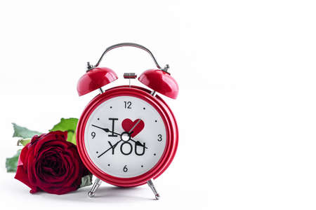 Red alarm clock with one rose on a white background. Greeting card for Valentines Day. Copy space.の写真素材