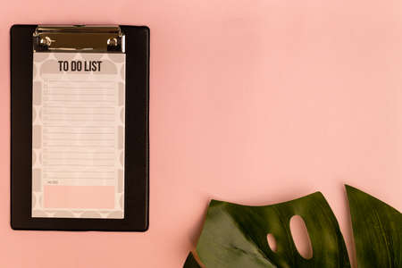 clipboard and monstera leaf on pink background. Flat lay, top view, copy space.