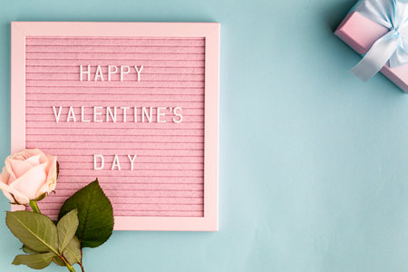 Festive composition with one rose and a box with a gift on a blue background. Top view, flat lay. Copy space.の写真素材