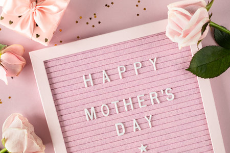 Happy mothers day words on pink felt letter board. Festive composition with roses and a box with a gift on a pink background. Top view, flat lay. Copy space.の写真素材