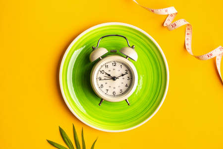 Composition with plate, alarm clock and measuring tape on a colored background. Diet concept and...