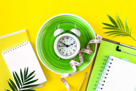 Composition with plate, alarm clock and measuring tape on a colored background.