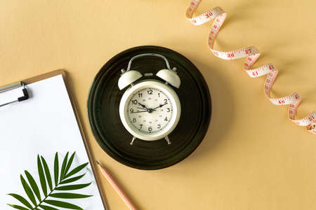 Composition with plate, alarm clock and measuring tape on a colored background.