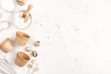 Paper molds for Baking cupcakes on a white concrete background and ingredients: Flour, Eggs, cane...