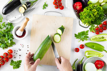 Step 2. Different vegetables. A healthy diet. Ingredients for baking. Vegetable ratatouille on a white background. Hands in the frame. Top viewの写真素材