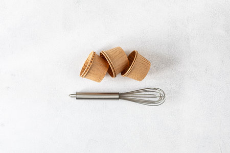 The concept of homemade baking is a whisk for whipping and cupcake molds on a white background. Zero...