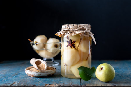 STEWED PEARS. Pears with spices in syrup in a jar on a dark background. Delicious dessert for the...