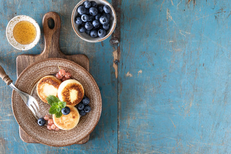 Cottage cheese pancakes, cheesecakes, ricotta fritters with fresh blueberries, currants and peaches on a plate. Healthy and delicious breakfast for the holiday. Blue wooden background. top viewの写真素材