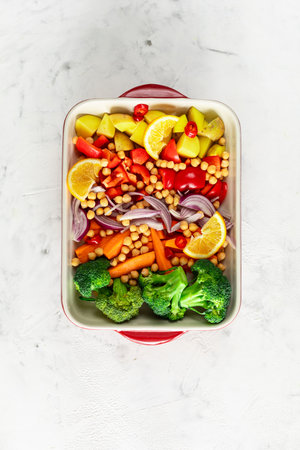 Raw peppers, potatoes, broccoli, chickpeas and onions with oil and spices in a baking dish. Top viewの写真素材