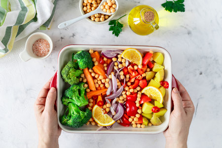 Raw peppers, potatoes, broccoli, chickpeas and onions with oil and spices in a baking dish. Top viewの写真素材
