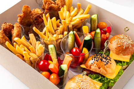 Food delivery. junk fast food in Eco Friendly Box: burger, French fries, strips, fresh tomatoes and cucumbers on a white background. Burger in EcoFriendly Box with Salad and French Fries on the Sideの写真素材