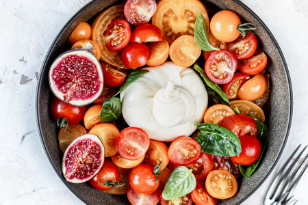 Delicious burrata cheese with fresh tomatoes, spinach, figs and olive oil. Round soft cheese with a liquid stracciatella texture inside. Top viewの写真素材