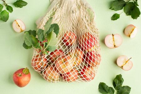 Delivery of vegetarian products. Bag with red apples on a light green background, top view