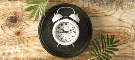 a retro alarm clock and a branch of a tropical palm tree on a wooden background, top view, bannerの写真素材