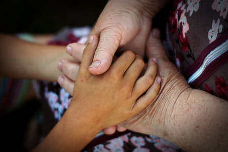 Grandmother and granddaughter hold hands together. The grandson's hands hold the wrinkled hand of an elderly grandmother. The concept of love and care.の写真素材