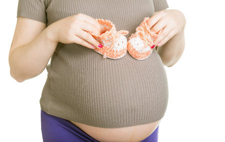 Pregnant woman holding baby's bootees on a white backgroundの写真素材