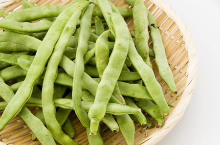 Flat green beans on bamboo sieve on white background