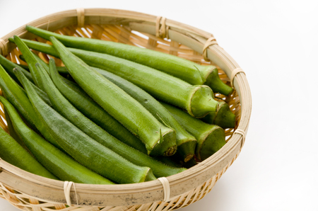 fresh okra in bamboo sieve isolated white backgroundの写真素材