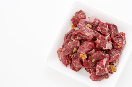 Seasoned raw chopped beef meat pieces on stainless steel tray on white background. Chuck eye roll.の写真素材