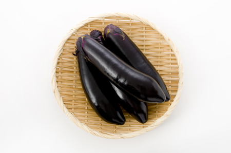 Raw black eggplant on bamboo sieve on white backgroundの写真素材
