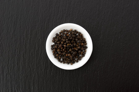 Black pepper in a white dish on black stone plateの写真素材