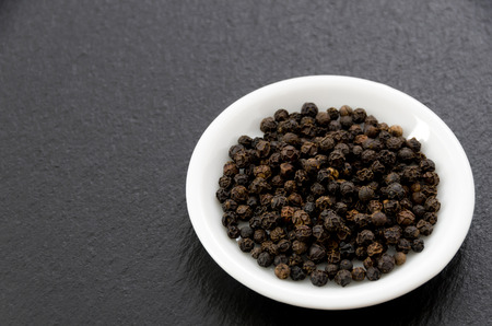 Black pepper in a white dish on black stone plateの写真素材