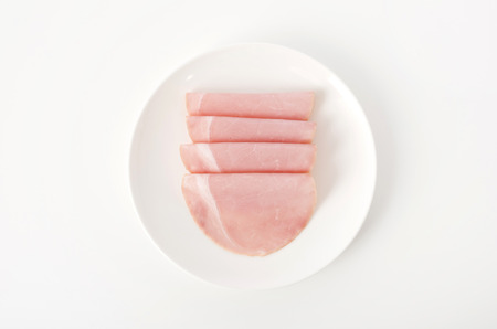 slices of pork loin ham on a dish on white backgroundの写真素材