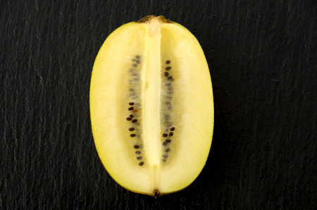 Half of fresh yellow-gold Kiwis on black stone plateの写真素材
