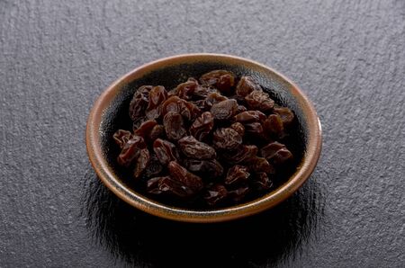 Raisins in small dish on black stoneの写真素材