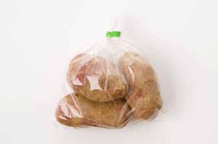 fresh red skinned potatoes with soil in plastic bag on white backgroundの写真素材