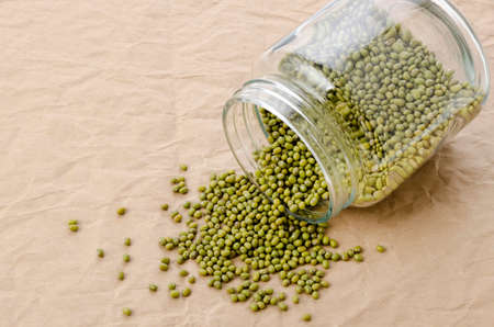 mung beans spilling out of a glass food jar on brown Paper backgroundの写真素材