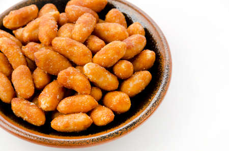Honey roasted peanuts in a black plate on white background